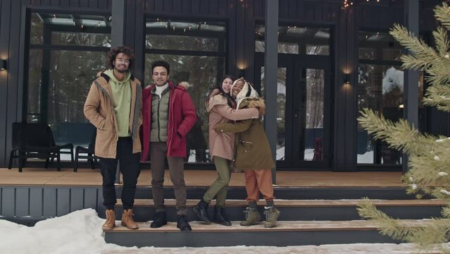 Slowmo long shot portrait of four ethnically diverse male and female friends standing outdoor on winter day smiling at camera