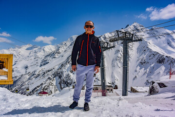 A man on the background of a gondola cable car and the snow-capped mountains of Elbrus. 2019 Russia.