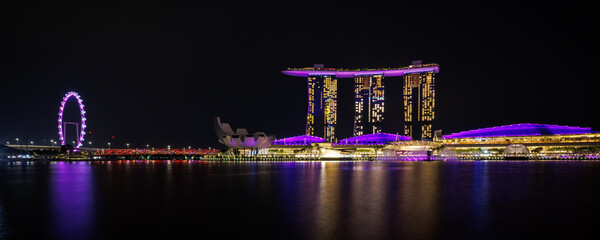 Cityscape in panorama view of night time urban skyscraper with light reflection on the water at Marina bay at Waterfront, Marina bay, Singapore. Tourist spot and attraction. - obrazy, fototapety, plakaty