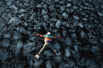 a man in ice skates lies on the transparent ice of the lake, view from above, aerial photography