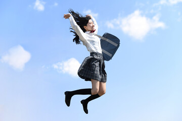 青空の下でジャンプをする笑顔の女子学生
