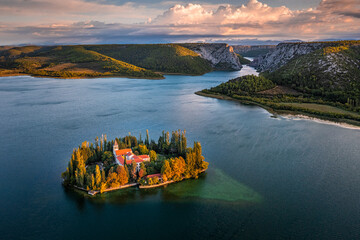Visovac, Croatia - Aerial view of Visovac Christian monastery island in Krka National Park on a sunny autumn morning with dramatic golden sunrise, autumn foliage and clear turquoise blue water - obrazy, fototapety, plakaty