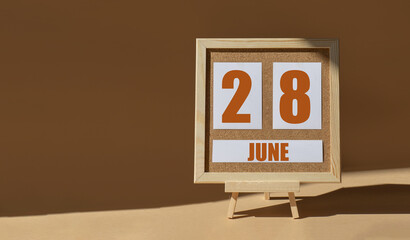 June 28th. Day 28 of month, Calendar date. Cork board, easel in sunlight on desktop. Close-up, brown background. Summer month, day of year concept