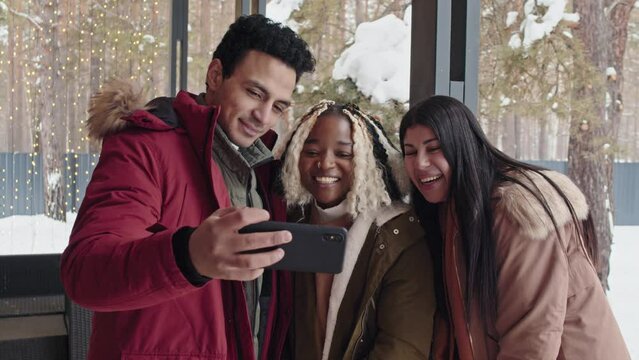Group of three multi-ethnic friends standing on porch shooting video for blog or having video call on smartphone