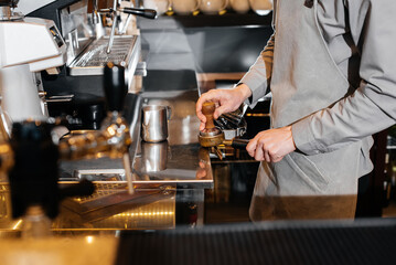 Close-up of a masked bartista preparing delicious delicious coffee at the bar in a coffee shop. The...