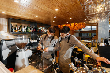 Two masked baristas prepare exquisite delicious coffee at the bar in the coffee shop. The work of restaurants and cafes during the pandemic.