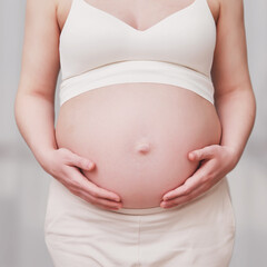 A pregnant woman in white clothes holds her stomach with her hands