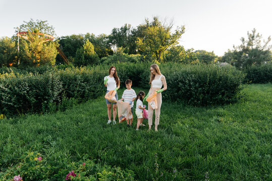 A Group Of Adults And Children Together At Sunset Is Engaged In Garbage Collection In The Park. Environmental Care, Waste Recycling. Sorting Garbage.