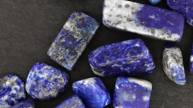 Lapis lazuli heap up jewel stones texture on black stone background. Moving right seamless loop backdrop.