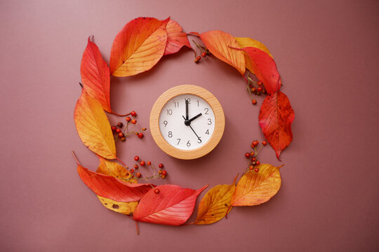 Fall time change still life with colorful tree foliage and wooden frame clock. Fall back concept background. A Clock and fallen leaves composition on brown background.