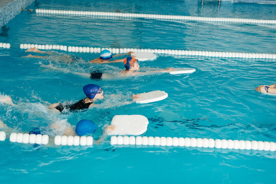 A group of boys and girls train and learn to swim in a modern swimming pool with an instructor. Development of children's sports. Healthy parenting and promotion of children's sports.