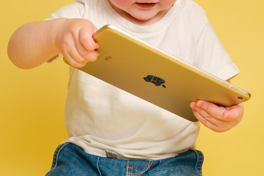 Toddler Baby With Apple IPad Digital Tablet On Studio Yellow Background. Happy Child Playing With A Tablet In A White T-shirt And Blue Jeans - Moscow, Russia, October 31, 2021