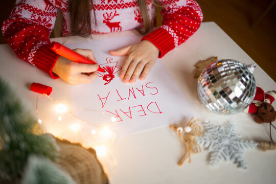 child draws santa claus on christmas letter with inscription dear santa. girl paints with marker