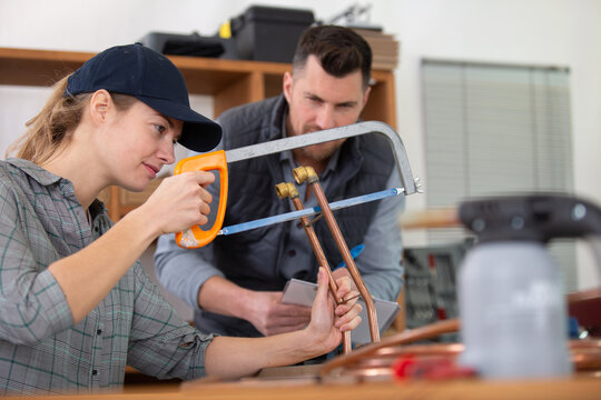 female worker using hacksaw to cut copper pipe