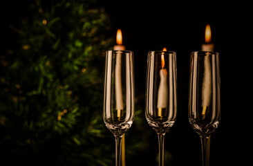Three champagne glasses with Christmas tree and lightning candles against black background