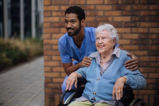 Happy senior woman at wheelchair spending time outside with her assistant.