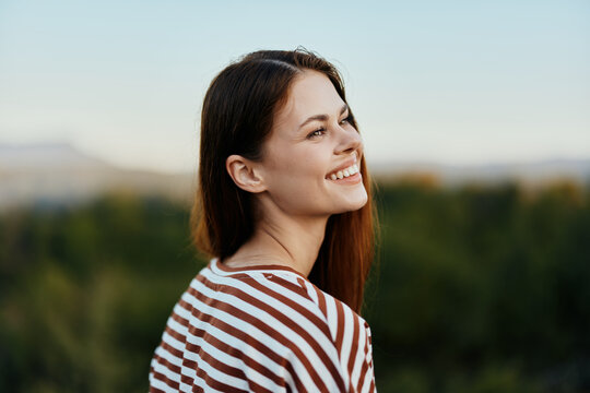 Close-up portrait of a young woman with a beautiful smile with teeth in a striped t-shirt against the background of trees