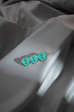 Close-up shot of a gold barrette with three turquoise hearts with rose decoration. The hair clip is isolated on a gray background. Top view.