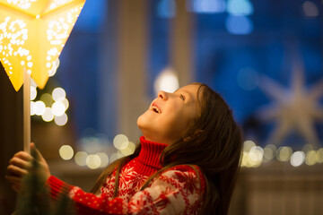 child at home rejoices at Christmas decor - lamp in form of star