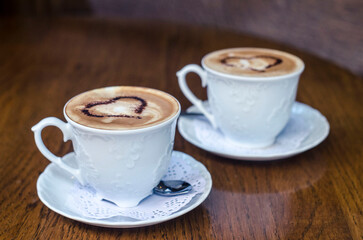 Two cups of coffee with pictures of hearts on a wooden vintage table.