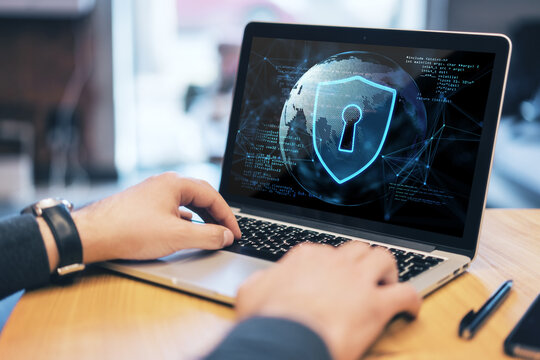 Close up of businessman hand using laptop keyboard at wooden desktop with abstract safety hologram with globe and coding on blurry background. Secure, protection and web concept. Double exposure.