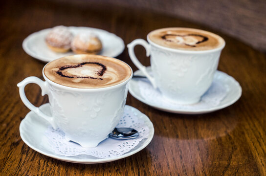 Two cups of coffee with pictures of hearts and a nut cake on a wooden table.
