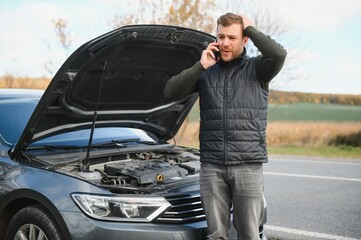 Handsome young man calling for assistance with his car broken down by the roadside