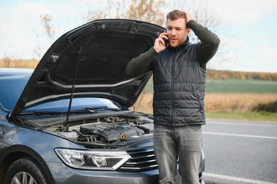 Handsome young man calling for assistance with his car broken down by the roadside