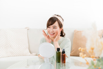 Fototapeta na wymiar 鏡を見ながら化粧品・コスメで保湿する日本人女性 