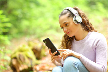 Fototapeta na wymiar Woman listening music wathing phone content in a forest