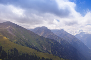 Mountain summer landscape. Snowy mountains and green grass. Peak Karakol Kyrgyzstan. Beautiful view from the top of the mountain