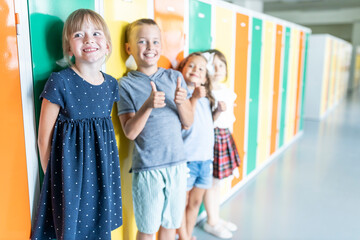 Happy elementary students standing near colorful lockers in school corridor
