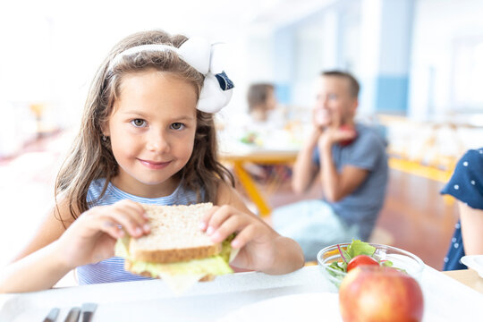 Smiling girl holding sandwich in school cafeteria