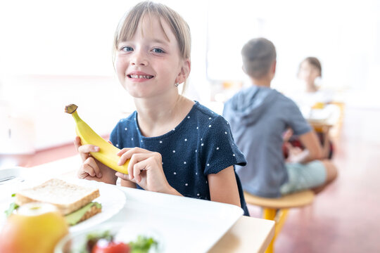 Smiling student holding fresh banana at lunch break in cafeteria