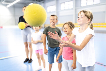 Smiling girl catching ball with friends at school sports court