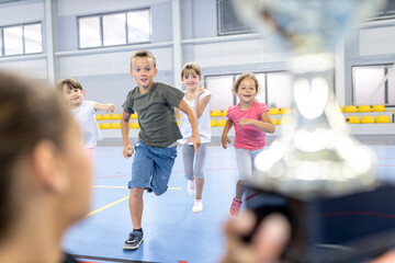 Excited students running towards trophy held by teacher at school sports court