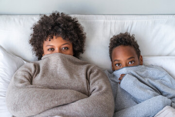 Mother and son covering mouth with sweater lying on bed at home