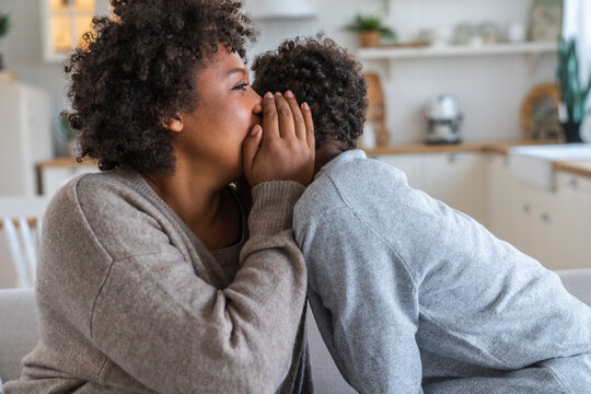 Mother whispering in son's ear at home