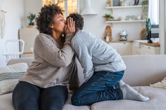 Mother whispering into son's ear at home