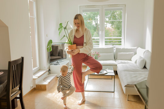 Boy with mother holding monstera plant standing in living room at home