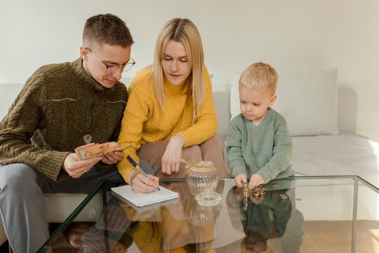 Young man and woman with son counting currency on table at home