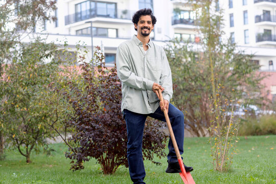 Smiling man with shovel standing by plant in garden