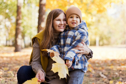 Cute boy with mother holding yellow leaves in park