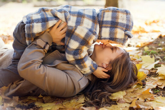 Mother kissing son lying on autumn leaves in park