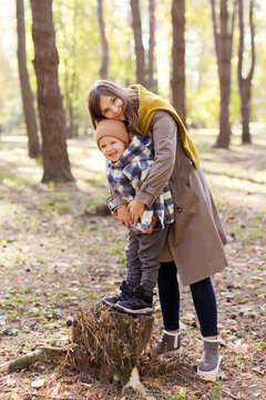 Happy boy standing on tree stump with mother in park