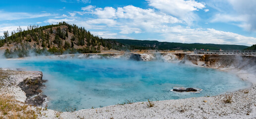 Beautiful panoramic view of smoke emitting from Excelsior geyser. Geothermal landscape and mountains with cloudy sky in background. Famous sightseeing attraction at Yellowstone national park.