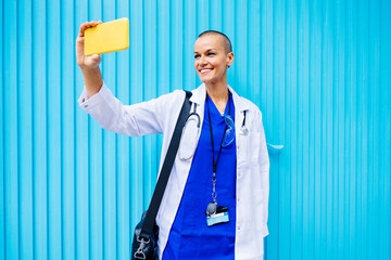 Smiling doctor talking selfie on smart phone with blue corrugated wall