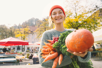 Smiling woman holding fresh vegetables showing pumpkin at market