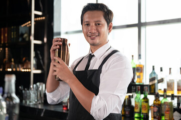 Asia Bartender holding steel cocktail shakers at the bar counter for preparing cocktail with city background at hotel
