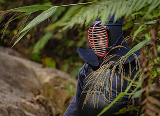 Portrait of kendoka man in the forest holding the sinai-sword behind a plant. Kendo is the Japanese martial art of sword fighting